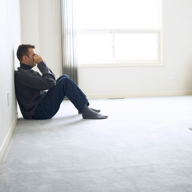 nešťastný muž sedí na zemi opretý o stenu