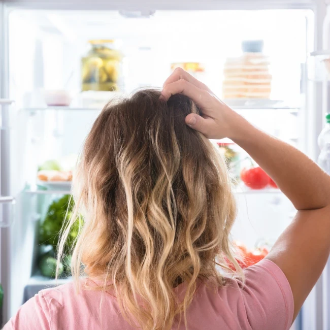 Žena hľadajúca jedlo v otvorenej chladničke ako symbol vlčieho hladu. Krabičková diéta EasyDiet predchádza nárazovému hladu vďaka pravidelnej strave.