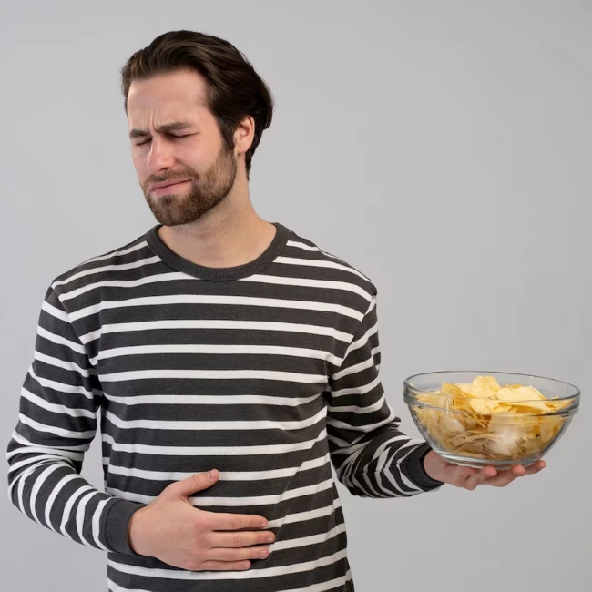 Muž v čiernobielom pásikavom tričku s bolesťou brucha drží v ruke misku s chipsami