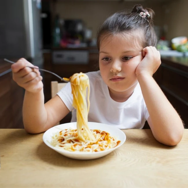 Das Mädchen sitzt gelangweilt in der Küche am Tisch über einem Teller voller Spaghetti