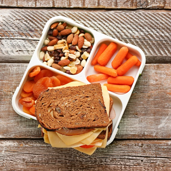 krabička na cesty obsahuje oriešky, sušené marhule, baby mrkvu a celozrnný sendvič so šunkou a syrom