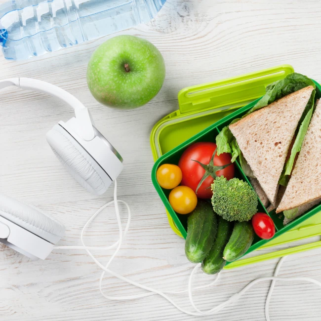 jablko, fľaša na vodu a zelený desiatový box so sendvičom, uhorkou, paradajkou a brokolicou