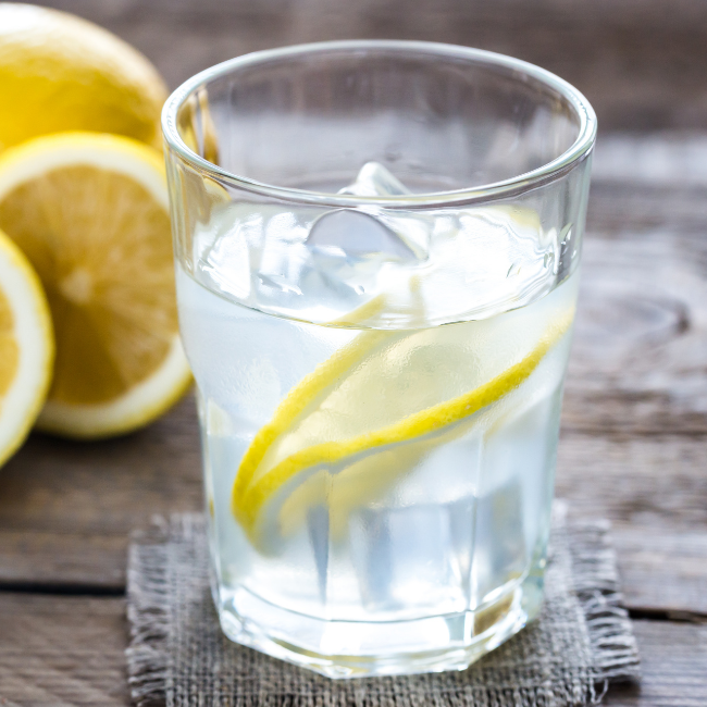 Pohár vody s kúskom citróna a ľadom položený na drevenom stole