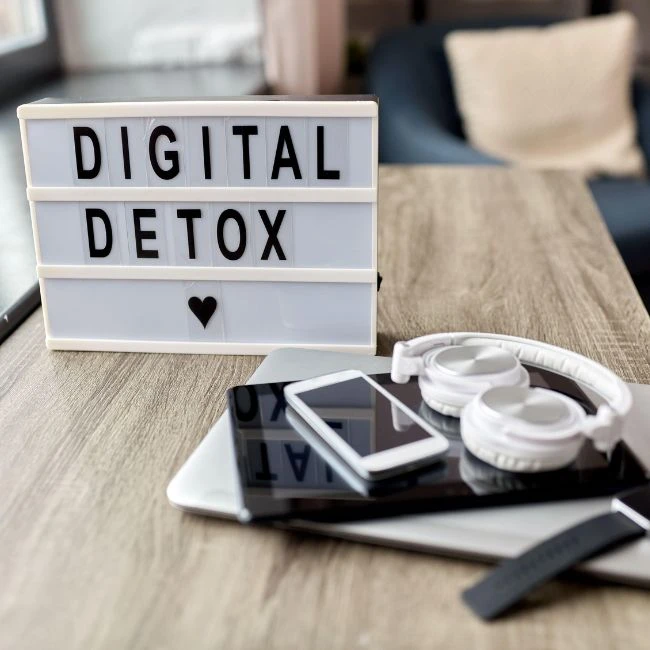 Schild mit der Aufschrift „Digital Detox“, daneben liegen Tablet, Smartphone, Kopfhörer und Smartwatch.