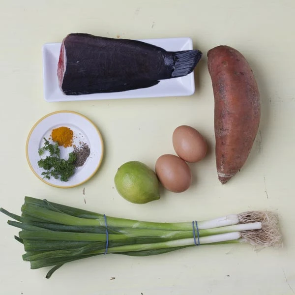 Zutaten auf hellem Hintergrund: Fisch, Süßkartoffel, Frühlingszwiebel, Eier, Limette und Gewürze.