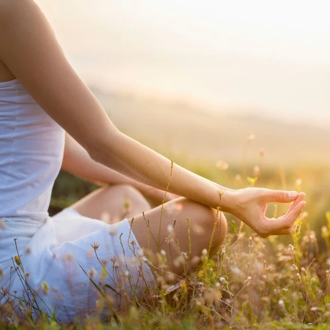Frau in weißer Kleidung meditiert auf einer Wiese.