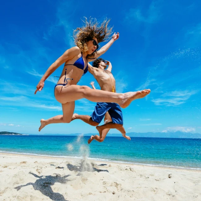 Frau und Mann in blauen Badeanzügen springen vergnügt am Strand.