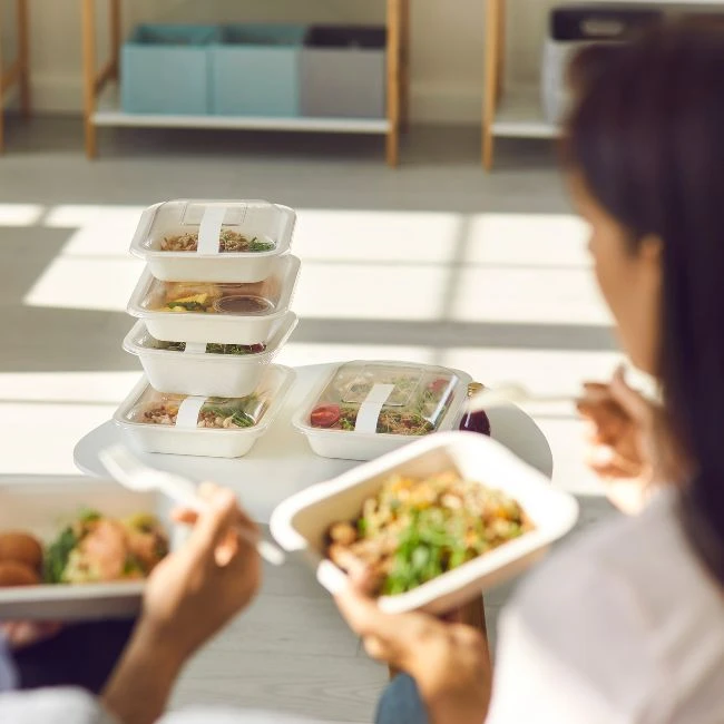 Zwei Frauen essen Box-Gerichte, vor ihnen stehen fünf Menüs einer Box-Diät.